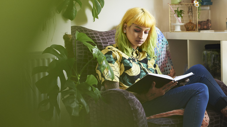 Girl with yellow and green hair reading a book at home