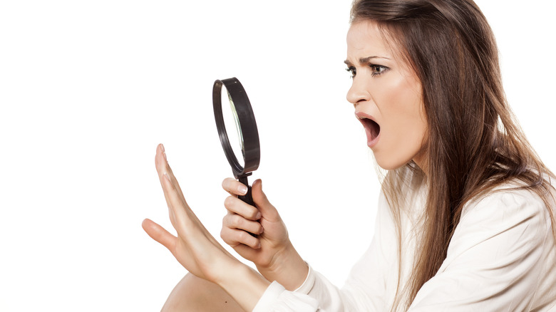 woman looking at her nails with a magnifying glass