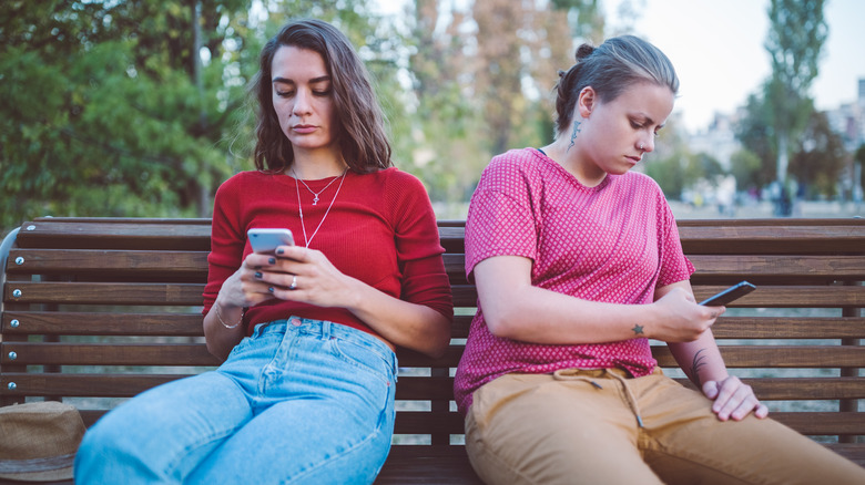 two women on a bench on phones
