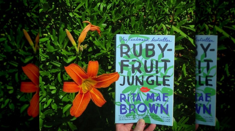 Hand holding "Rubyfruit Jungle" against greenery