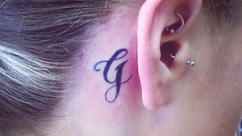 G initial behind ear tattoo