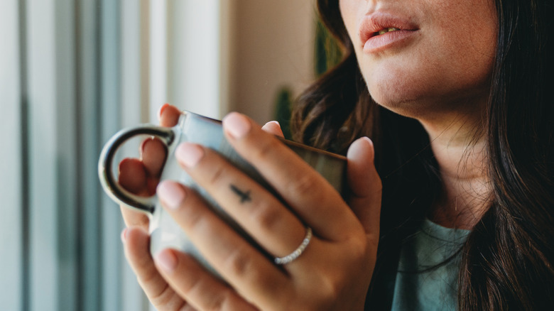 woman holding a mug with a cross tattoo on finger