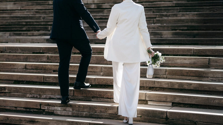 Bride in pantsuit with groom walking up steps