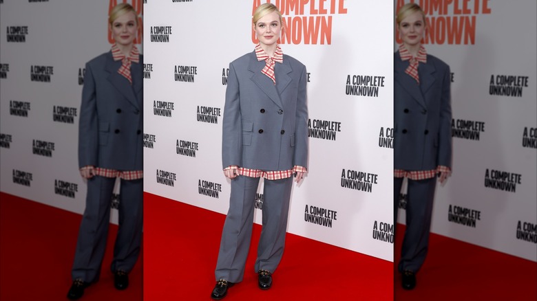 Elle Fanning in a grey suit and orange shirt at an event