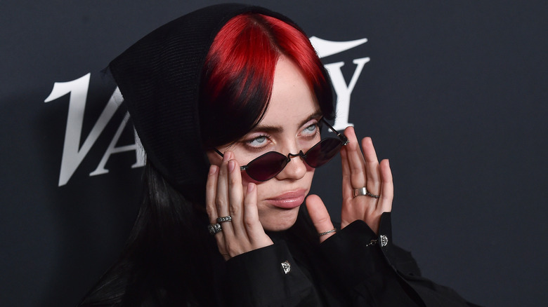 Billie Eilish with red roots and sunglasses, pouting on the red carpet