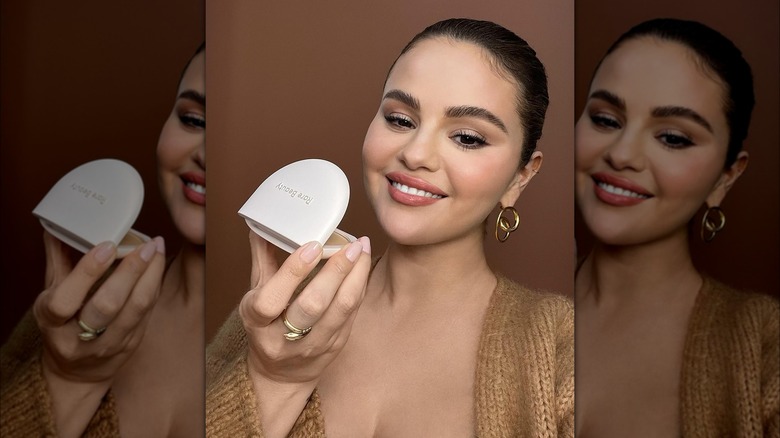 Selena Gomez in a bun holding up Rare Beauty makeup