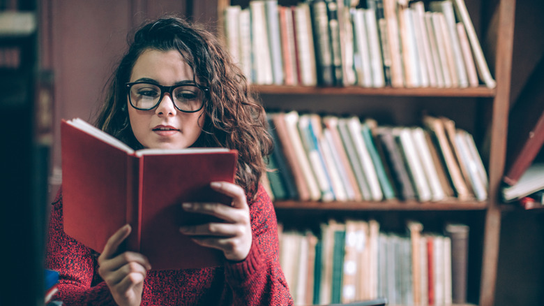 woman with glasses reading red book in library