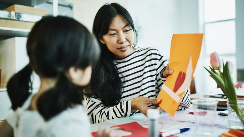 A mother and daughter sit at a table and work on a craft project together