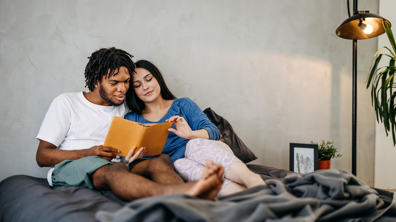 Interracial couple reading a book together in bed