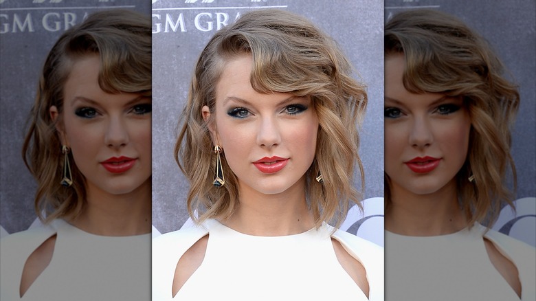 Taylor Swift looking into the camera with a small smile, wearing her hair side-parted with loose curls