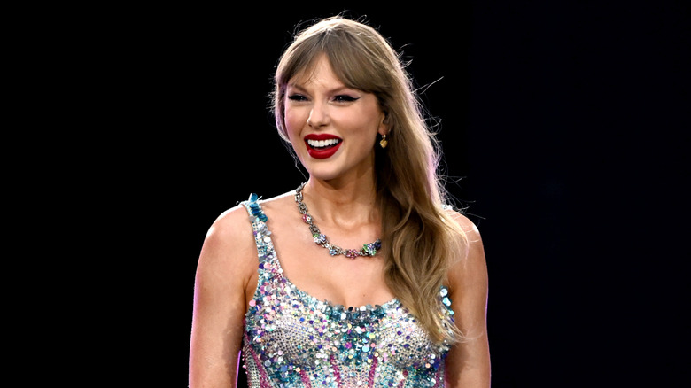 Taylor Swift smiling while getting emotional onstage at the Eras Tour, wearing her hair down with parted bangs