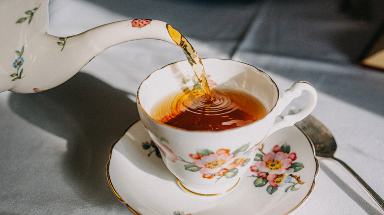 Close-up of a tea pot pouring tea into a flower-adorned tea cup