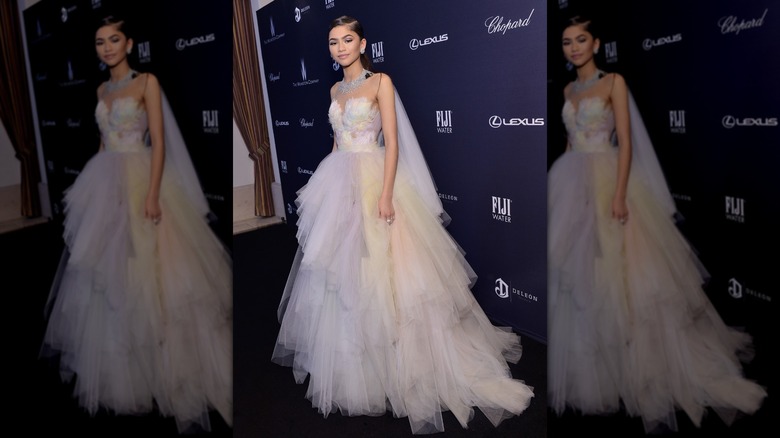 Zendaya posing with a small smile while wearing a tulle and feather gown