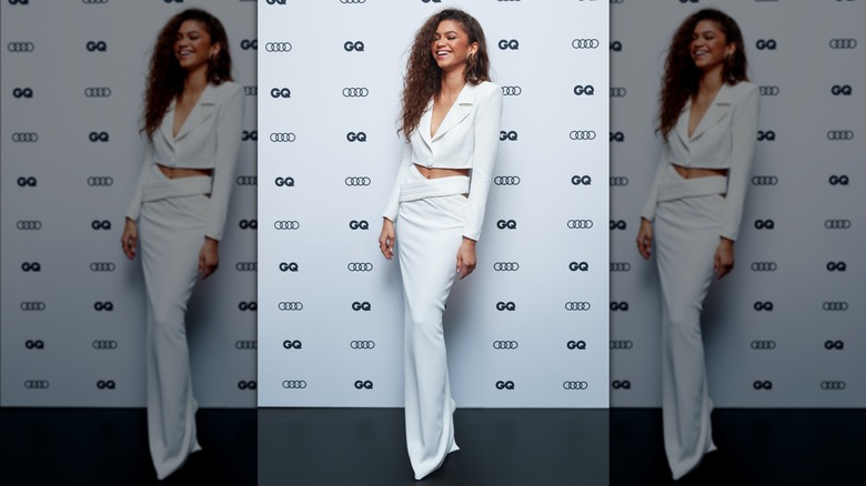 Zendaya laughing while wearing a monochrome blazer and skirt set