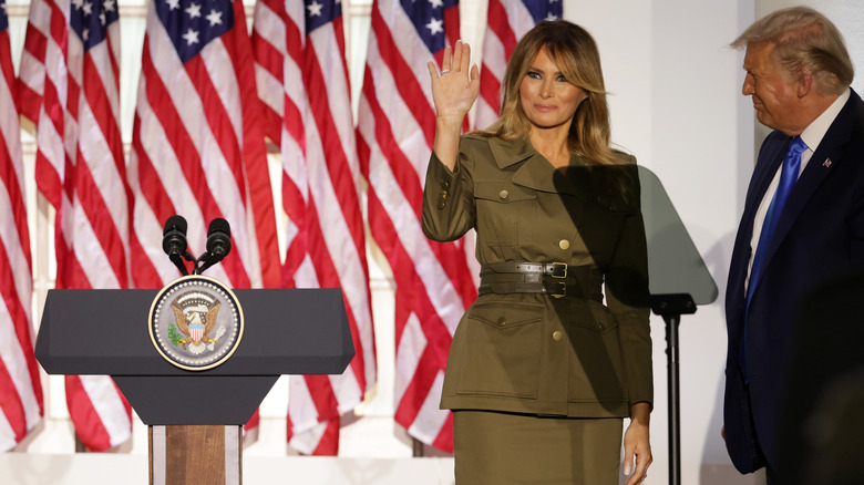 Melania Trump on stage waving in front of American Flags