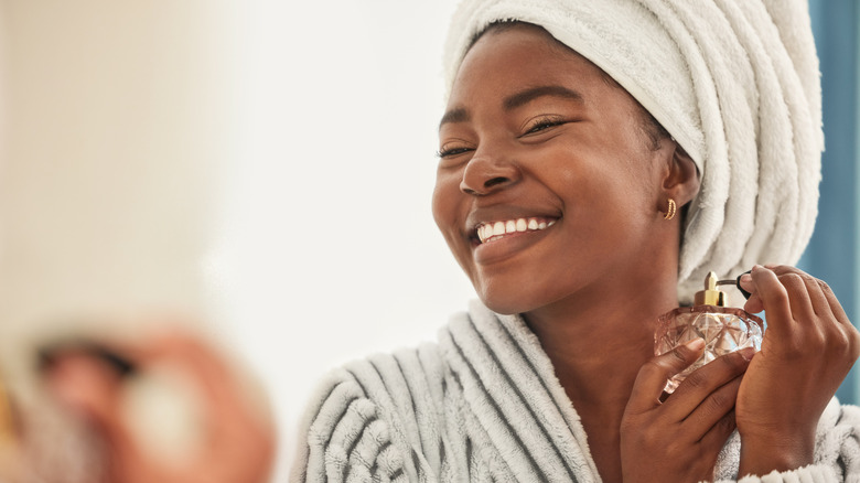 Woman in towel and bathrobe smiling and applying perfume