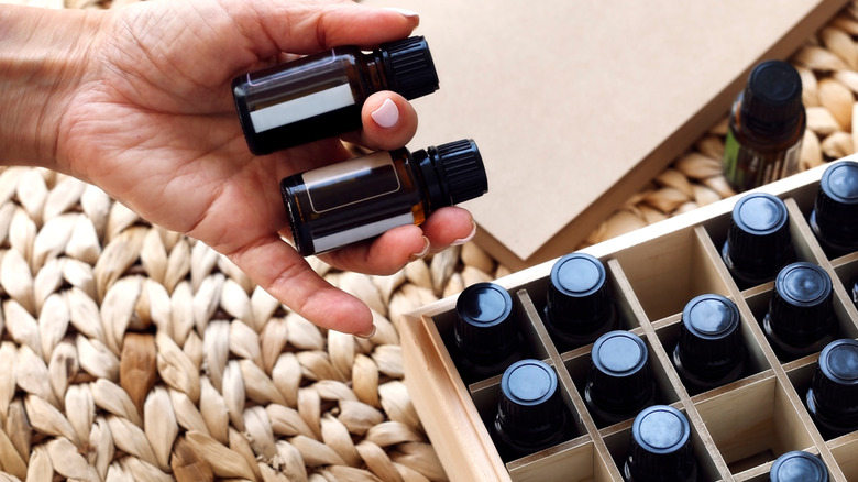 Hand holding two perfume oils while several others sit inside a wooden box