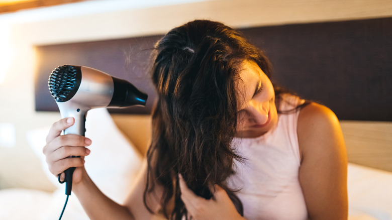 woman blow drying hair in bed