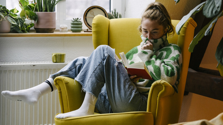 A woman is sitting comfortable on a chair reading a book