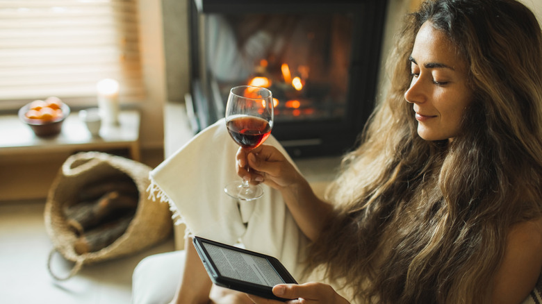 A woman holding a glass of wine while reading using an e-reader