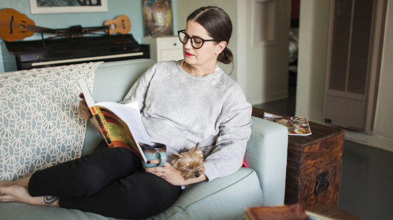 A woman cuddles her dog on the sofa while reading a book