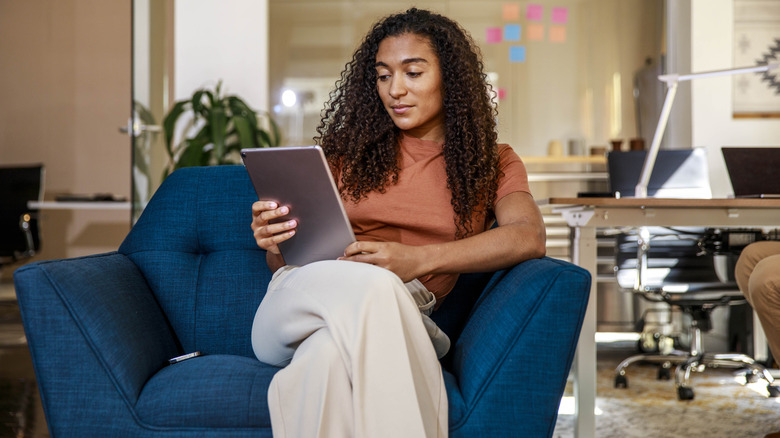 A woman is sitting comfortably on a couch and reading her tablet