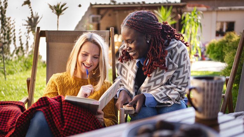 Two women sit together outside and look at a book together