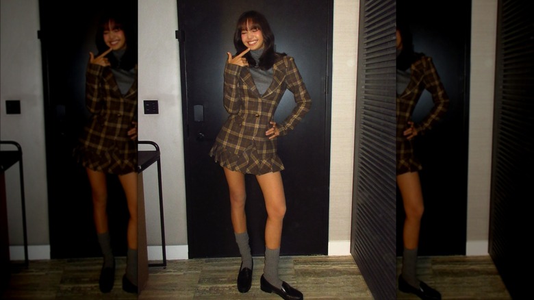 Lisa posing in front of a black door, wearing a matching plaid skirt and blazer