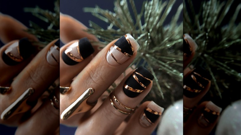 Nails with gold stripe decals against matte black and nude polish