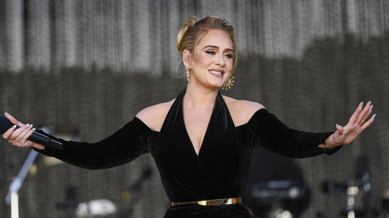 Adele on stage in a black dress with shoulder cut-outs