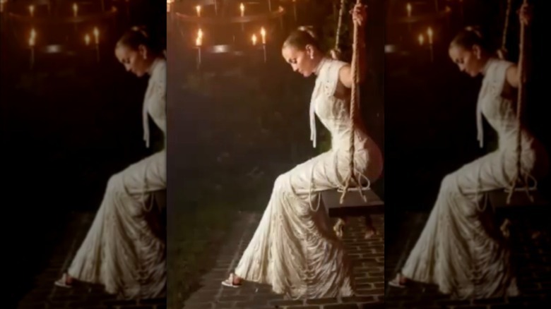 Jennifer Lopez sitting on a swing wearing a wedding gown draped in pearls