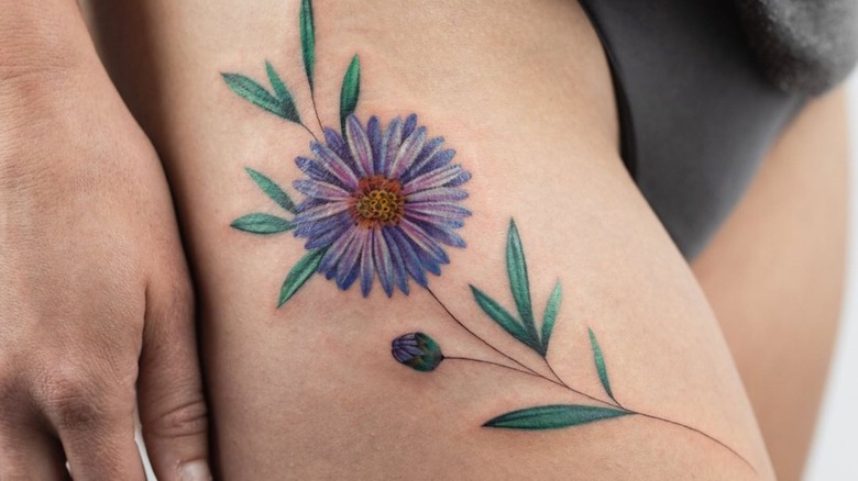 A colorful, large aster tattoo on the upper thigh 