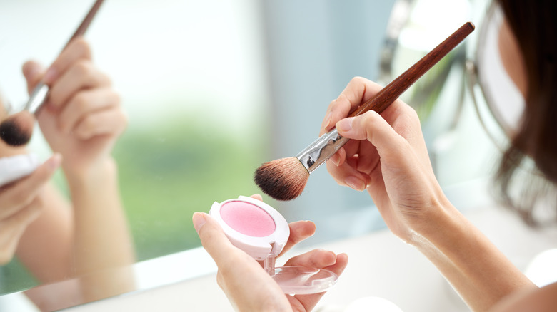 A person holding cream blush and brush