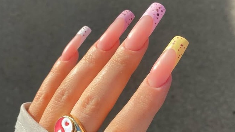 Close-up of a French manicure with pink, white, and yellow spotted nails