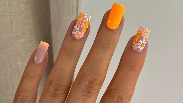 Orange manicure featuring two nails with white and orange flowers