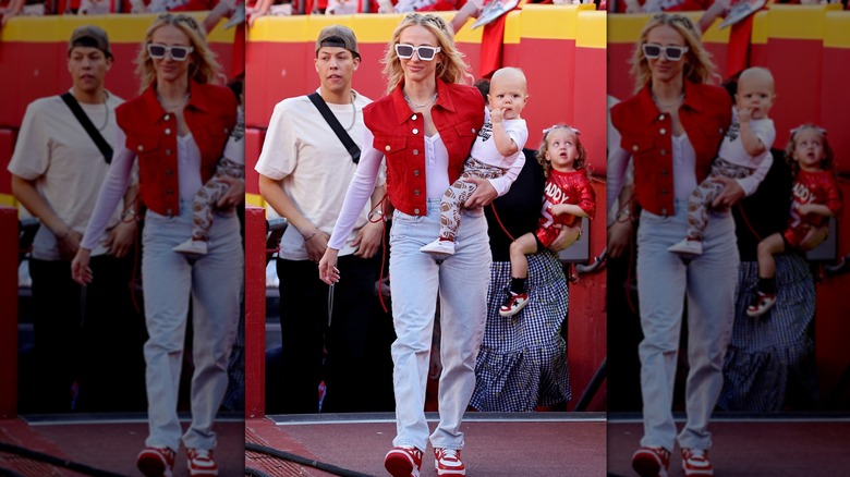 Brittany Mahomes in baggy jeans and a red vest holding her baby at a game