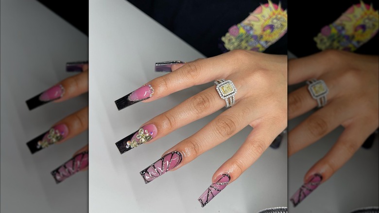 Hand with ring and purple and black butterfly square-tip nails.