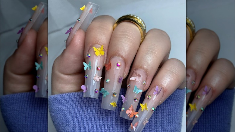 Hand showing clear, long nails with 3D butterfly art