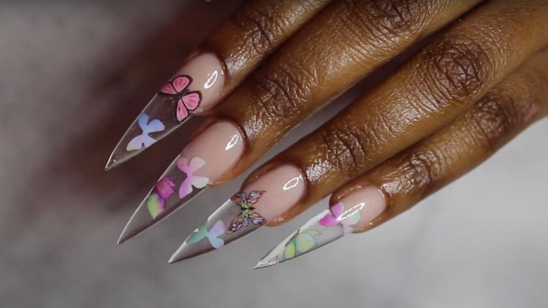 Clear stiletto acrylic nails with colorful butterfly decals.