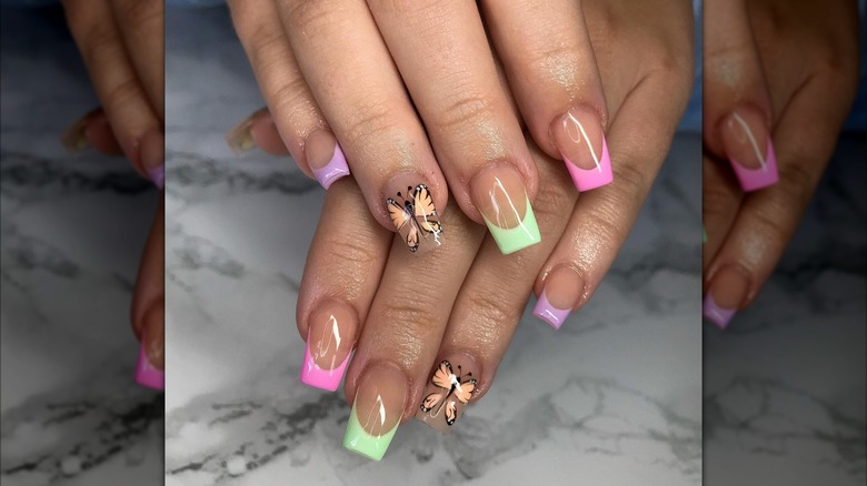 A woman's hands with pastel tipped nails and butterflies