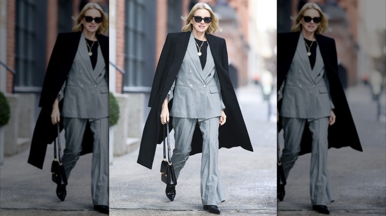 Naomi Watts wearing a grey suit and black trench while walking in New York City