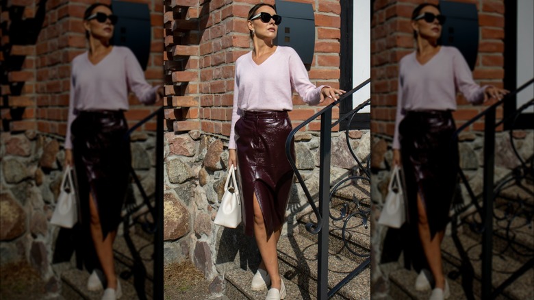 A woman standing outside in a cherry skirt, a pink sweater and white shoes