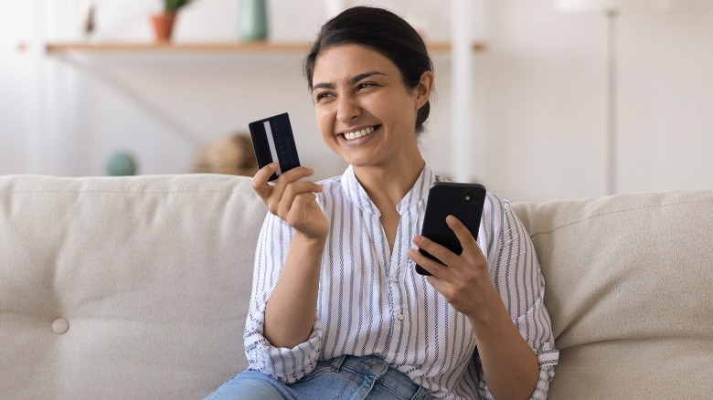 Woman smiles holding debit card and phone