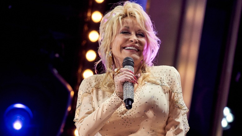 Dolly Parton on smiling on stage holding a microphone