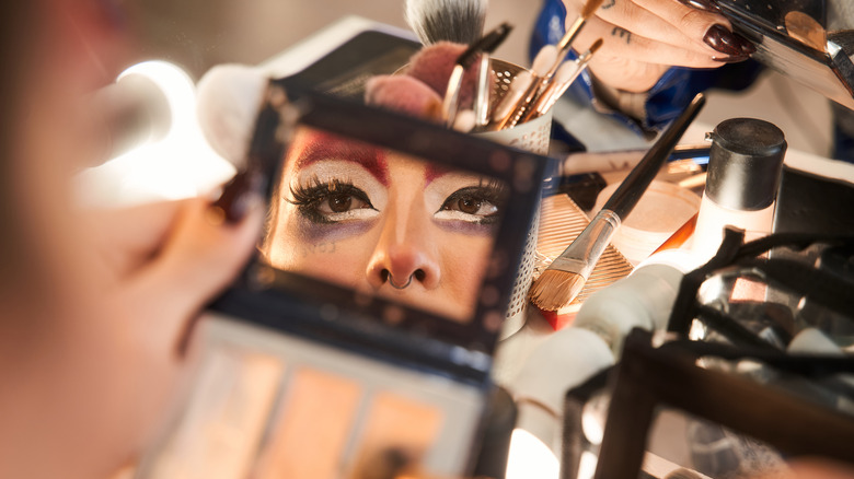 Drag queen applying makeup in mirror