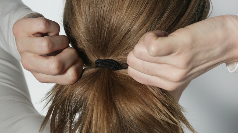 woman tying hair in ponytail 