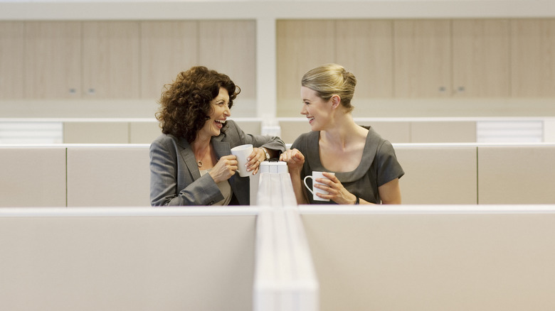 Two women laughing over coffee in office