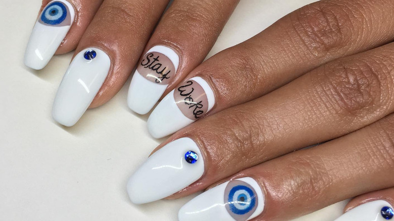 Manicure with 'stay woke' and evil eye fingernail tattoos with white gel polish overlay