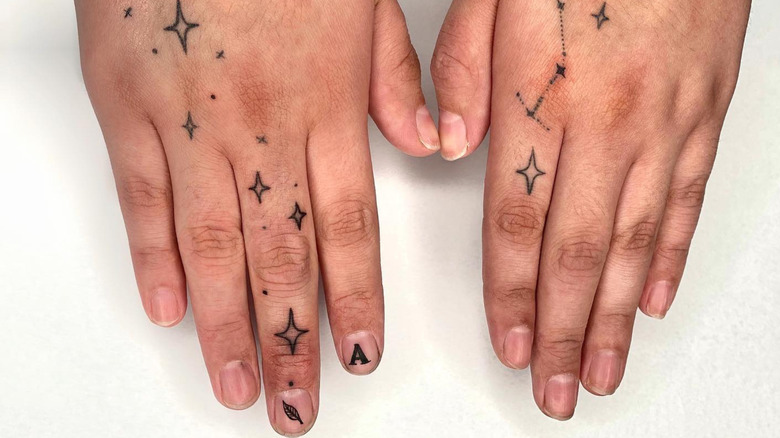 Small feather and 'A' fingernail tattoos next to starburst hand tattoos
