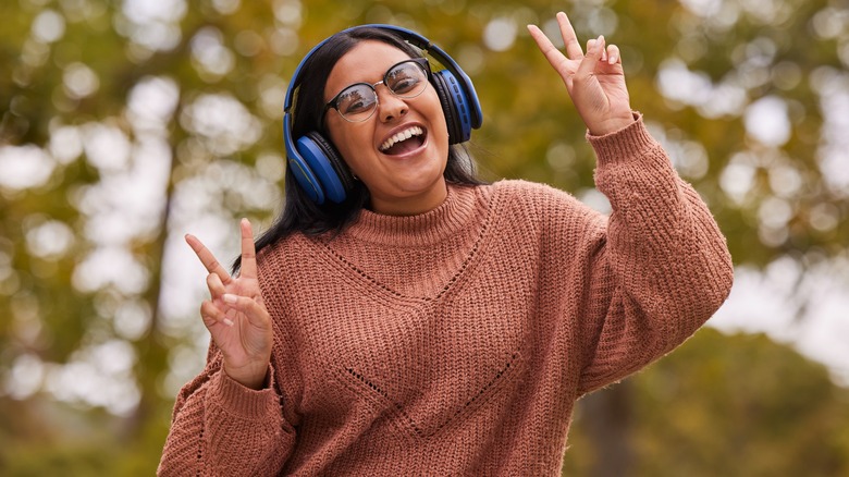 A woman wearing earphones flashes peace signs on a hike